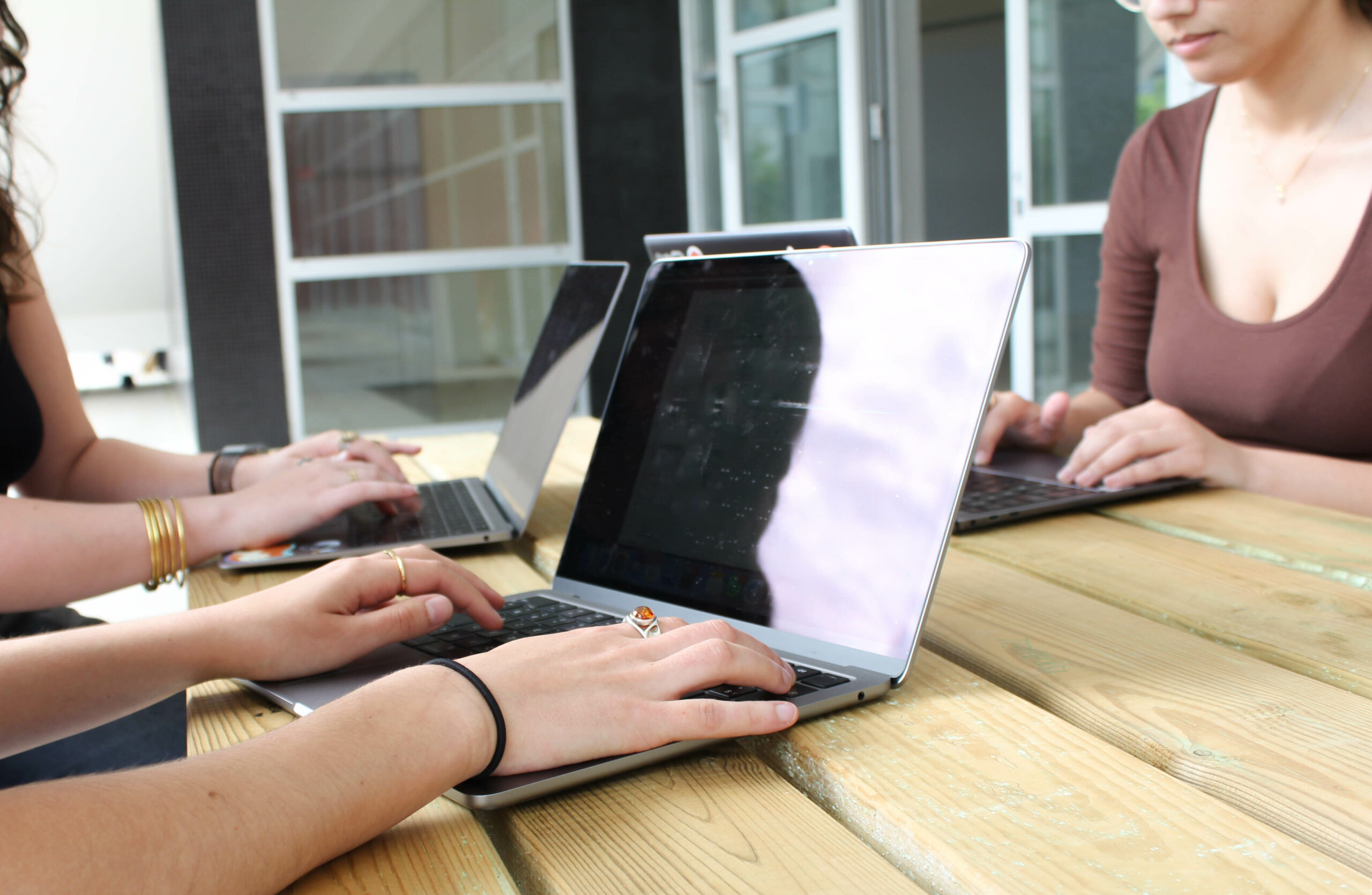 Trois étudiantes en Master Caweb communication web multilingue travaillant dehors sur une table en bois