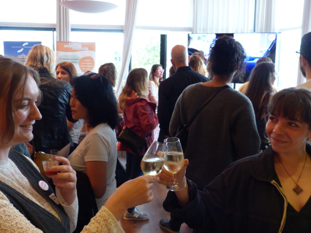 Students and alumni of the CAWEB Master’s program toast with drinks, celebrating the program's 20th anniversary in a lively indoor gathering.